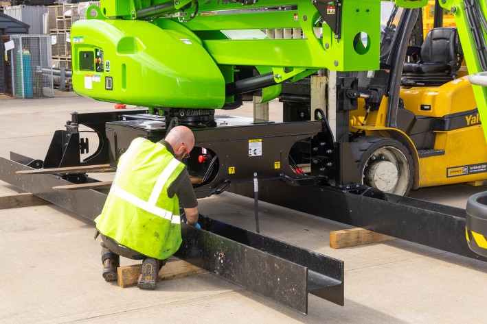DeckRider® conversion in progress Niftylift technician fitting a steel skid assembly during a DeckRider conversion, with the machine supported by a forklift