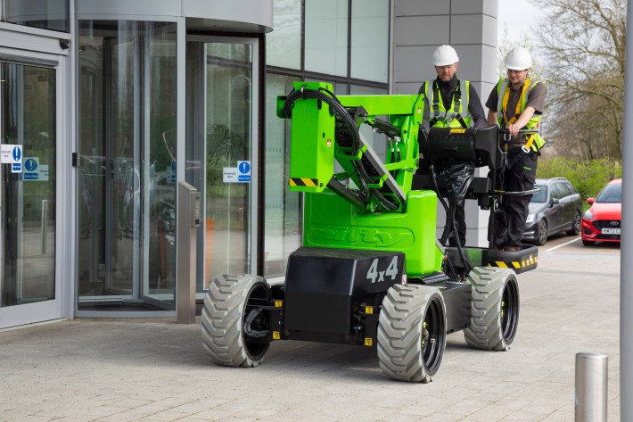 HR12 4x4 driving on paving slabs with two people in the platform outside an office entrance
